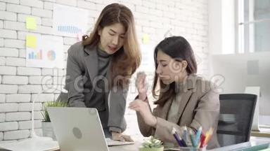 <strong>两</strong>位年轻的亚洲女商人在小<strong>企业</strong>的办公室里一起工作，高兴地坐在那里阅读报告或文件。
